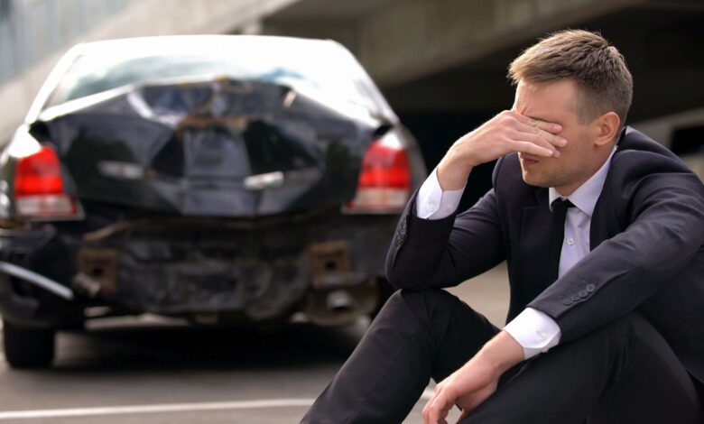 Desperate man sitting asphalt on crashed car background, automobile accident