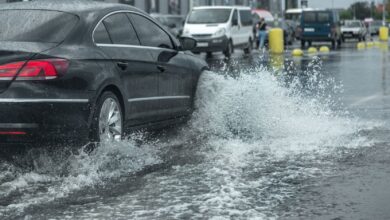 Driving car on flooded road during flood caused by torrential rains. Cars float on water, flooding streets. Splash on the car. Flooded city road with a large puddle