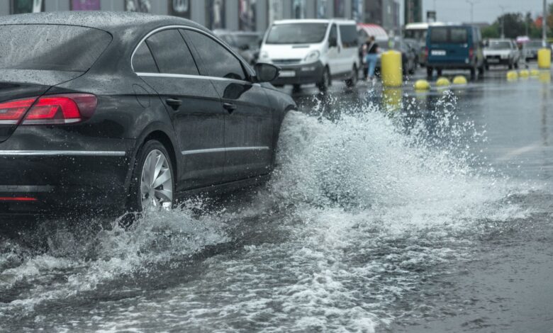 Driving car on flooded road during flood caused by torrential rains. Cars float on water, flooding streets. Splash on the car. Flooded city road with a large puddle
